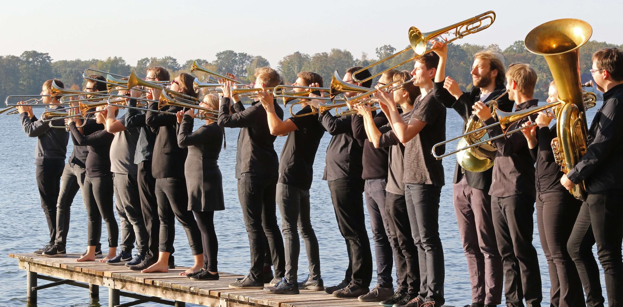 Der Landesjugendposaunenchor mit Trompeten, Posaunen und Tuba auf einem Steg am See.